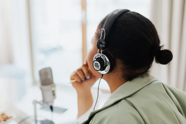 A woman wearing headphones is engaged in podcasting indoors by a window. Audio-Kampagnen messen
