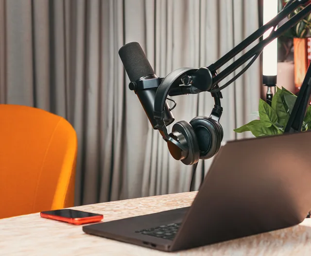 Modern podcasting studio with mic, headphones, laptop, and smartphone on a wooden table. Audio-Werbebudgets